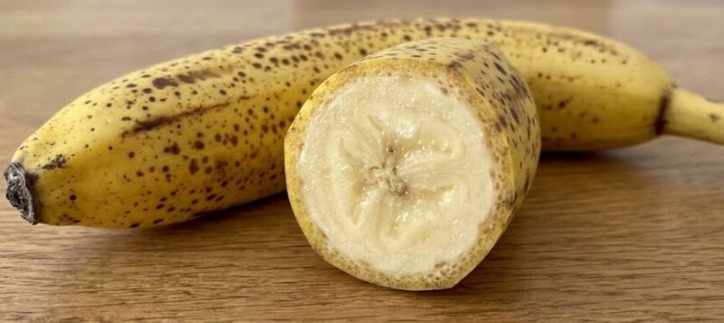全体に茶色のシュガースポット（黒い斑点）が現れた完熟バナナと、その断面のクローズアップ写真。断面は蜜を含んだように透明感があり、果肉が詰まっている様子がわかる。