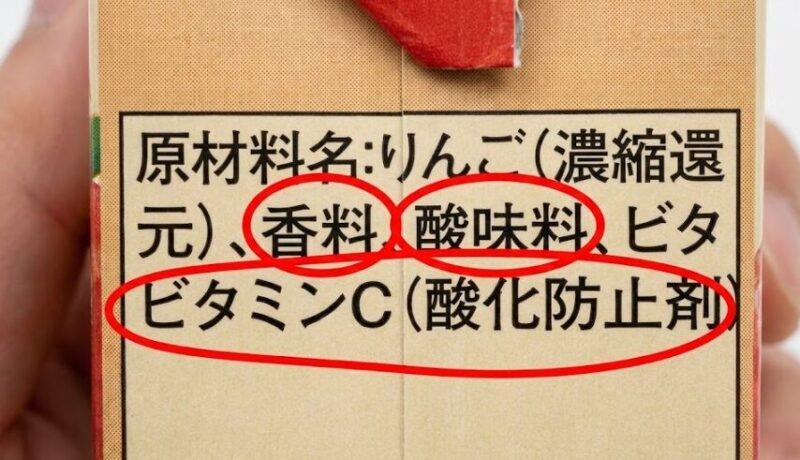 市販の濃縮還元ジュースの原材料名ラベル。「香料」「酸味料」「ビタミンC（酸化防止剤）」が赤丸で強調